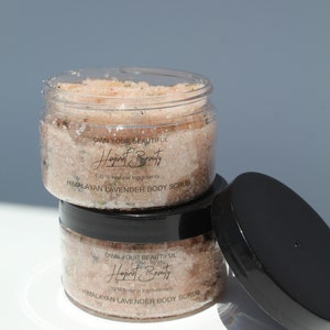 May include: Two clear jars of Himalayan Lavender Body Scrub with black lids. The jars are stacked on top of each other. The label on the front of the jars reads "Own Your Beautiful Hajinat Beauty 100% Natural Ingredients Himalayan Lavender Body Scrub 4 oz."