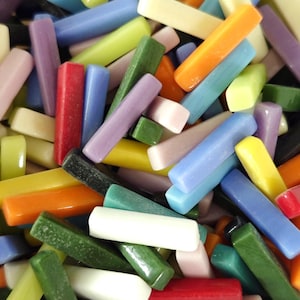 Könnte beinhalten: Eine Sammlung kleiner, rechteckiger Glasfliesen in verschiedenen Farben, darunter Rot, Orange, Gelb, Grün, Blau, Violett, Weiß und Schwarz. Jede Fliese hat eine glatte, glänzende Oberfläche und abgerundete Kanten und ist in einem dichten Haufen angeordnet.