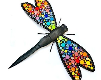 Puede incluir: Un kit de libélula de mosaico colorido. La libélula está hecha de metal negro y tiene alas cubiertas de azulejos de mosaico de colores. El kit incluye todos los materiales necesarios para crear la libélula.