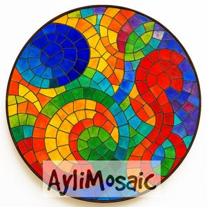Peut inclure: Une œuvre d'art en mosaïque circulaire avec un motif coloré de motifs en spirale dans des tons de rouge, orange, jaune, vert, bleu et violet. La mosaïque est faite de petites tuiles carrées et est encadrée dans un bois brun foncé.