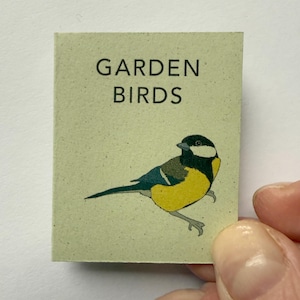 May include: A small, rectangular card with the words "GARDEN BIRDS" printed in black. The card features a colorful illustration of a bird with yellow, black, and blue plumage. The bird is perched on a light green background.
