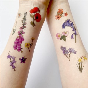 May include: Two arms displaying temporary floral tattoos. The designs feature red poppies, purple foxgloves, yellow buttercups, and bluebells. Other flowers include daisies, and a sprig of lavender. The tattoos are colourful and detailed.