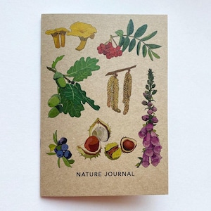 May include: A nature journal with a brown cover featuring botanical illustrations of mushrooms, berries, acorns, and flowers. The words "NATURE JOURNAL" are printed at the bottom of the cover.