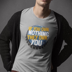 May include: A gray t-shirt with a blue and yellow graphic of a bottle cap that says "If you own nothing they own you".