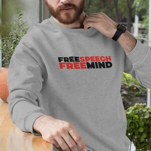 Puede incluir: Una sudadera gris con el texto "FREESPEECH FREEMIND" impreso en letras negras y rojas.