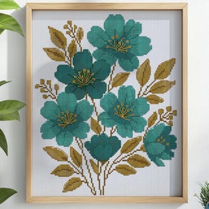 Op de afbeelding: Een ingelijst kruissteek bloemenontwerp met turquoise bloemen met gouden centra en bladeren. Het kunstwerk staat tegen een witte achtergrond en is omlijst in licht hout. De tekst "DESIGNFOR CROSSSTITCH" is rechtsonder zichtbaar.