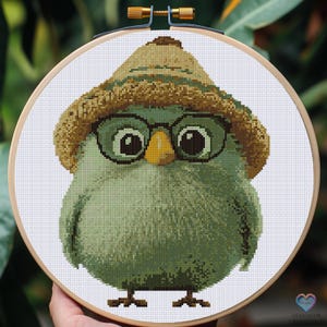 Puede incluir: Un búho verde con un sombrero marrón y gafas redondas. El búho tiene ojos grandes y redondos y un pequeño pico amarillo.