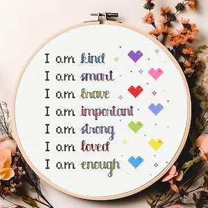 Puede incluir: Un aro de bordado blanco con la frase "Soy amable, soy inteligente, soy valiente, soy importante, soy fuerte, soy amado, soy suficiente" bordada en hilo de colores con un pequeño corazón después de cada frase.
