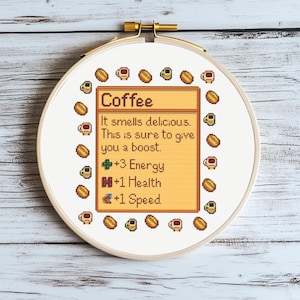 May include: A cross-stitch embroidery hoop with a coffee-themed design. The text reads "Coffee" and details its effects: +3 Energy, +1 Health, and +1 Speed. The design includes pixelated coffee cups and beans, all within a circular frame.