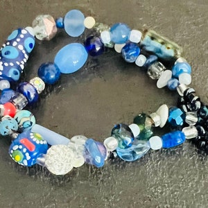 Peut inclure: Un bracelet en perles bleu et blanc avec différentes formes et tailles de perles, y compris une grosse perle bleue et blanche en forme d'œil.