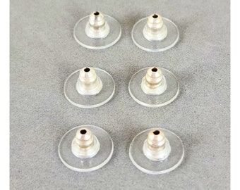 May include: Six silver ear backs for earrings. The ear backs are made of metal and have a clear plastic backing. The ear backs are arranged in two rows of three.
