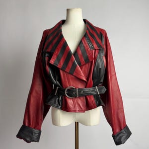 Leren jas uit de jaren 80 in rood en zwart, met een getailleerde ceintuur, een opvallend statement-item in de stijl van Mozart Co., glamrock en dramatisch maatwerk.