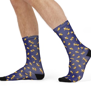 May include: A pair of navy blue socks with a repeating pattern of yellow bananas. The socks have black heels and toes. The socks are worn by a person.