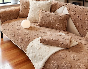 May include: A brown sofa with paw print pattern, featuring matching throw pillows and a blanket. The pillows are in shades of brown and cream. The sofa is in a living room setting with a plant and a lamp.