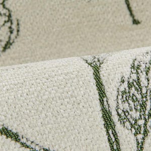 May include: Close-up of a textured, off-white fabric with a repeating green leaf pattern. The fabric is folded over, revealing the texture and design. The pattern appears to be printed or woven into the material.
