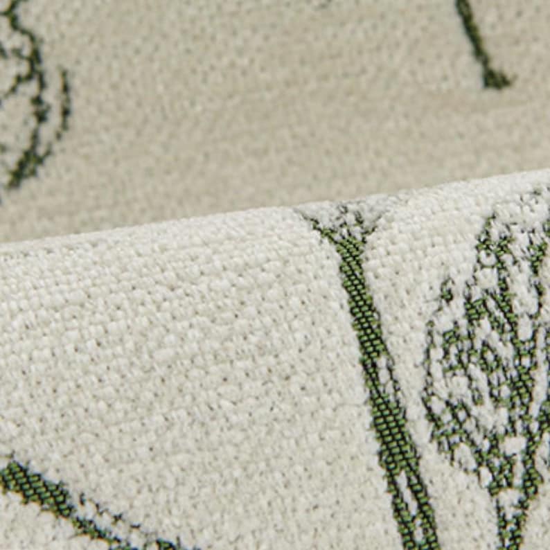 May include: Close-up of a textured, off-white fabric with a repeating green leaf pattern. The fabric is folded over, revealing the texture and design. The pattern appears to be printed or woven into the material.