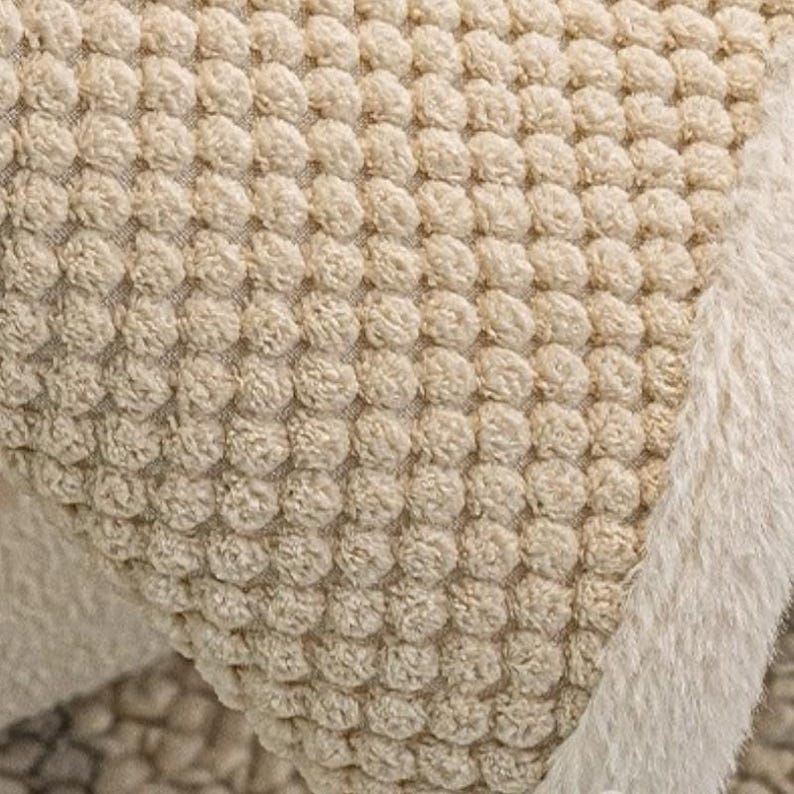 Pu&ograve; includere: Primo piano di un tessuto beige strutturato con un motivo ripetuto di piccole forme arrotondate in rilievo. Il tessuto ha un aspetto morbido e felpato. Un bordo soffice color crema borda il bordo del tessuto.