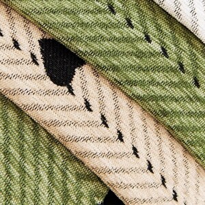 May include: Close-up of textured fabric in shades of green, beige, and white. The fabric has a diagonal pattern with black accents, including a large black shape. The image showcases the texture and color variations.