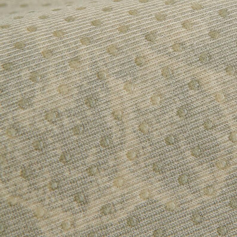 May include: Close-up of a textured fabric with a repeating pattern of small, raised dots. The fabric has a light beige color with subtle variations and a ribbed texture. The dots are a slightly darker shade.