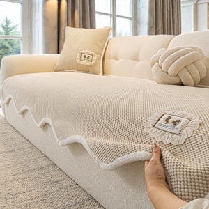 Pu&ograve; includere: Divano color crema con cuscini coordinati e una coperta in maglia. La coperta ha un bordo smerlato e una toppa decorativa con la scritta "carpe diem". I cuscini includono un cuscino a forma di nodo e un cuscino quadrato con una toppa decorativa.