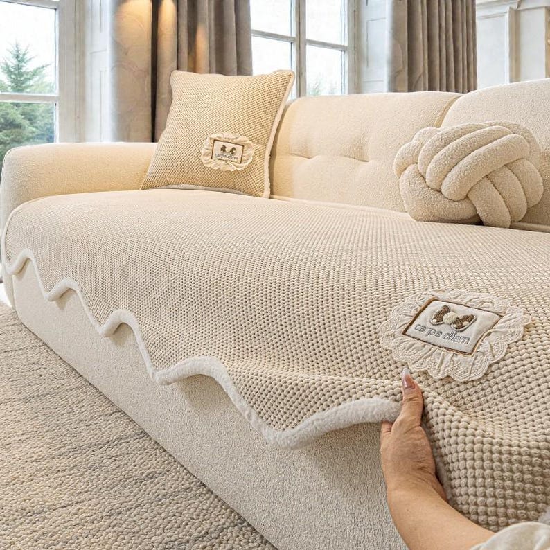 Pu&ograve; includere: Divano color crema con cuscini coordinati e una coperta in maglia. La coperta ha un bordo smerlato e una toppa decorativa con la scritta "carpe diem". I cuscini includono un cuscino a forma di nodo e un cuscino quadrato con una toppa decorativa.