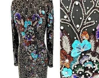 Könnte beinhalten: Schwarzes Abendkleid mit langen Ärmeln, verziert mit farbenfrohen Blumen- und Astmotiven. Das Kleid hat einen hohen Ausschnitt und einen Schlitz vorne. Die aufwendigen Perlen- und Pailletten-Details umfassen Blau-, Lila-, Braun- und Silbertöne.