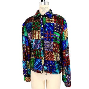 May include: A vintage sequined jacket in a patchwork design. The jacket features a variety of colors, including blue, green, red, and gold, arranged in a geometric pattern. It has a collared neckline, long sleeves, and gold buttons.