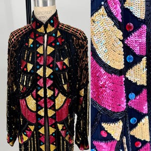 May include: A long, open black jacket heavily embellished with sequins and beads. The jacket features geometric patterns in gold, red, and teal, with a high collar and long sleeves. The intricate design is eye-catching and detailed.