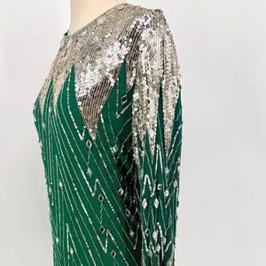 May include: Emerald green sequined dress with silver accents. The dress features a geometric pattern of silver sequins and beads, with long sleeves and a round neckline. A glamorous, vintage-inspired garment.