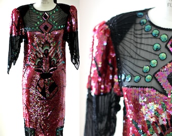 May include: A long-sleeved, sequined dress with a black mesh overlay. The dress is pink, green, and silver with a geometric pattern.