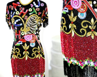 Puede incluir: Un vestido corto negro de lentejuelas con un estampado abstracto colorido, detalles dorados y una falda de cuentas rojas. El vestido tiene un dobladillo de flecos.