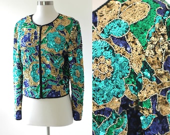 May include: A cropped sequined jacket with a floral pattern in shades of teal, green, gold, and blue. The jacket has a zipper closure and long sleeves.