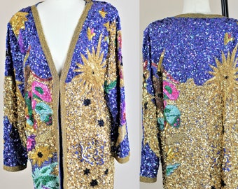 May include: A long-sleeved sequined cardigan with a V-neckline. The cardigan is decorated with a colorful, celestial design featuring a sun, stars, and other celestial bodies. The cardigan is primarily gold and blue with accents of pink, green, and purple.