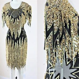 May include: A black and gold sequined dress with a short sleeve and a fringe hem. The dress is covered in sequins and beads.