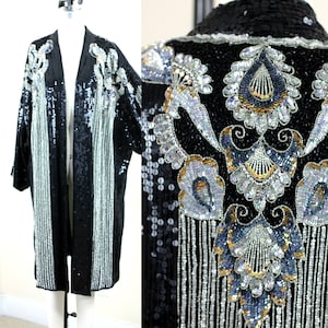 Può includere: Una giacca nera di paillettes con ricami argentati e dorati. La giacca ha un design lungo e fluido e un collo sciallato. La giacca è decorata con un motivo floreale e frange.