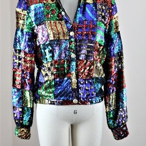 May include: A multi-colored sequined jacket with a patchwork design. The jacket has a button-up front and long sleeves. The sequins are in shades of red, green, blue, gold, and purple.