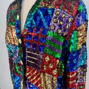 Puede incluir: Chaqueta de lentejuelas colorida con dise&ntilde;o de patchwork. La chaqueta presenta lentejuelas rojas, azules, verdes y doradas dispuestas en patrones geom&eacute;tricos. Tiene cuello en V y tres botones dorados. Una prenda llamativa.
