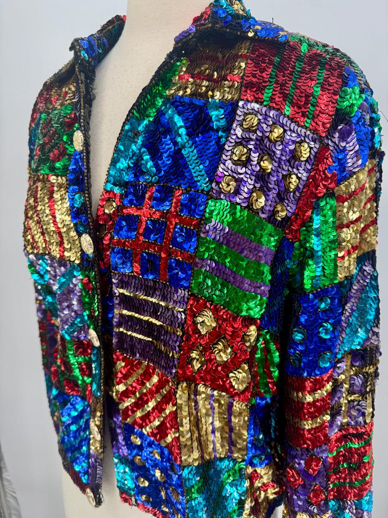 Puede incluir: Chaqueta de lentejuelas colorida con dise&ntilde;o de patchwork. La chaqueta presenta lentejuelas rojas, azules, verdes y doradas dispuestas en patrones geom&eacute;tricos. Tiene cuello en V y tres botones dorados. Una prenda llamativa.