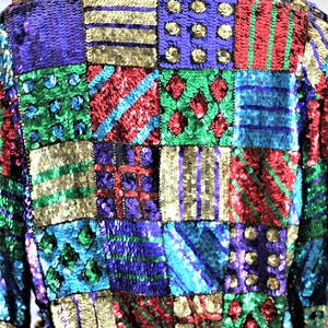 Puede incluir: Chaqueta de lentejuelas colorida con dise&ntilde;o de patchwork. La chaqueta presenta cuadrados de varios colores, incluyendo verde, morado, rojo y dorado. Las lentejuelas crean un efecto brillante, convirti&eacute;ndola en una pieza llamativa.