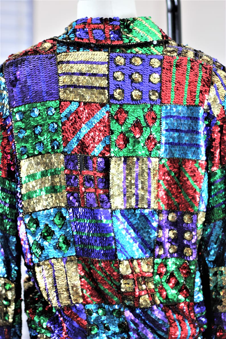 Puede incluir: Chaqueta de lentejuelas colorida con dise&ntilde;o de patchwork. La chaqueta presenta cuadrados de varios colores, incluyendo verde, morado, rojo y dorado. Las lentejuelas crean un efecto brillante, convirti&eacute;ndola en una pieza llamativa.