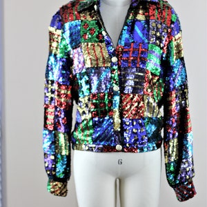 Puede incluir: Chaqueta de lentejuelas colorida con dise&ntilde;o de patchwork. La chaqueta tiene cuello, mangas largas y botones dorados. Las lentejuelas son en tonos rojo, azul, verde y dorado.