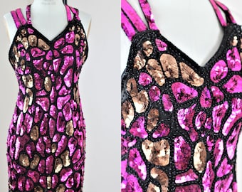 May include: A striking, sequined cocktail dress in fuchsia, black, and gold. The dress has a V-neck and halter straps. The body of the dress is covered in a mosaic pattern of sequins. A glamorous party dress.