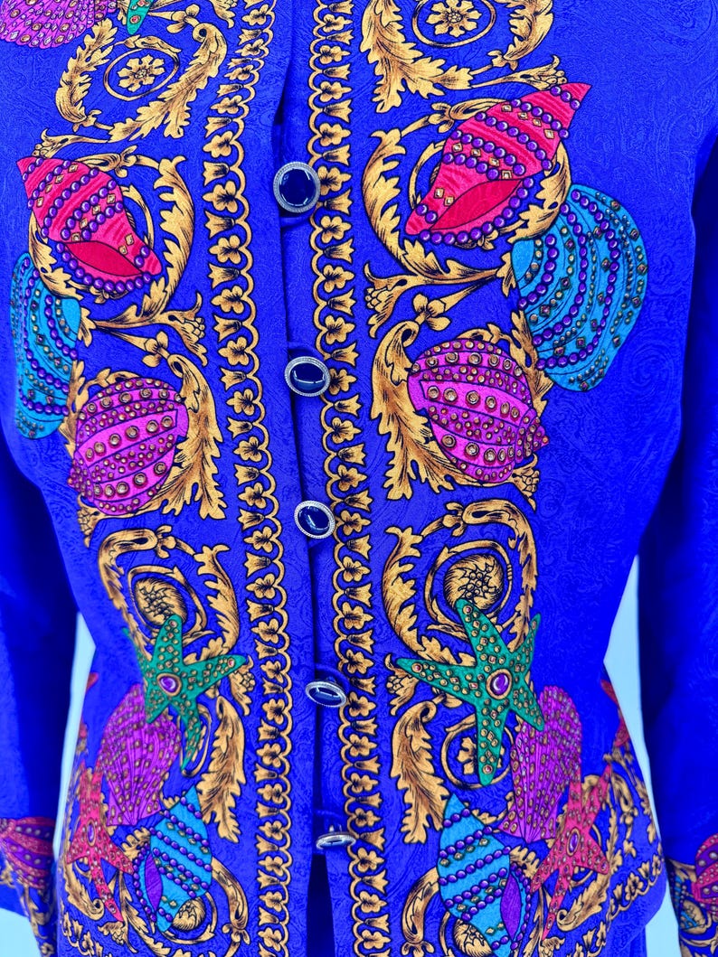 May include: A royal blue jacket with a detailed pattern of seashells, starfish, and ornate gold accents. The jacket features a button-up front with dark blue buttons. The design incorporates shades of pink, teal, and green.