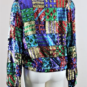 Puede incluir: Chaqueta de lentejuelas colorida con dise&ntilde;o de patchwork. La chaqueta presenta una variedad de colores, incluyendo azul, verde, rojo y dorado. La chaqueta se muestra en un maniqu&iacute;.
