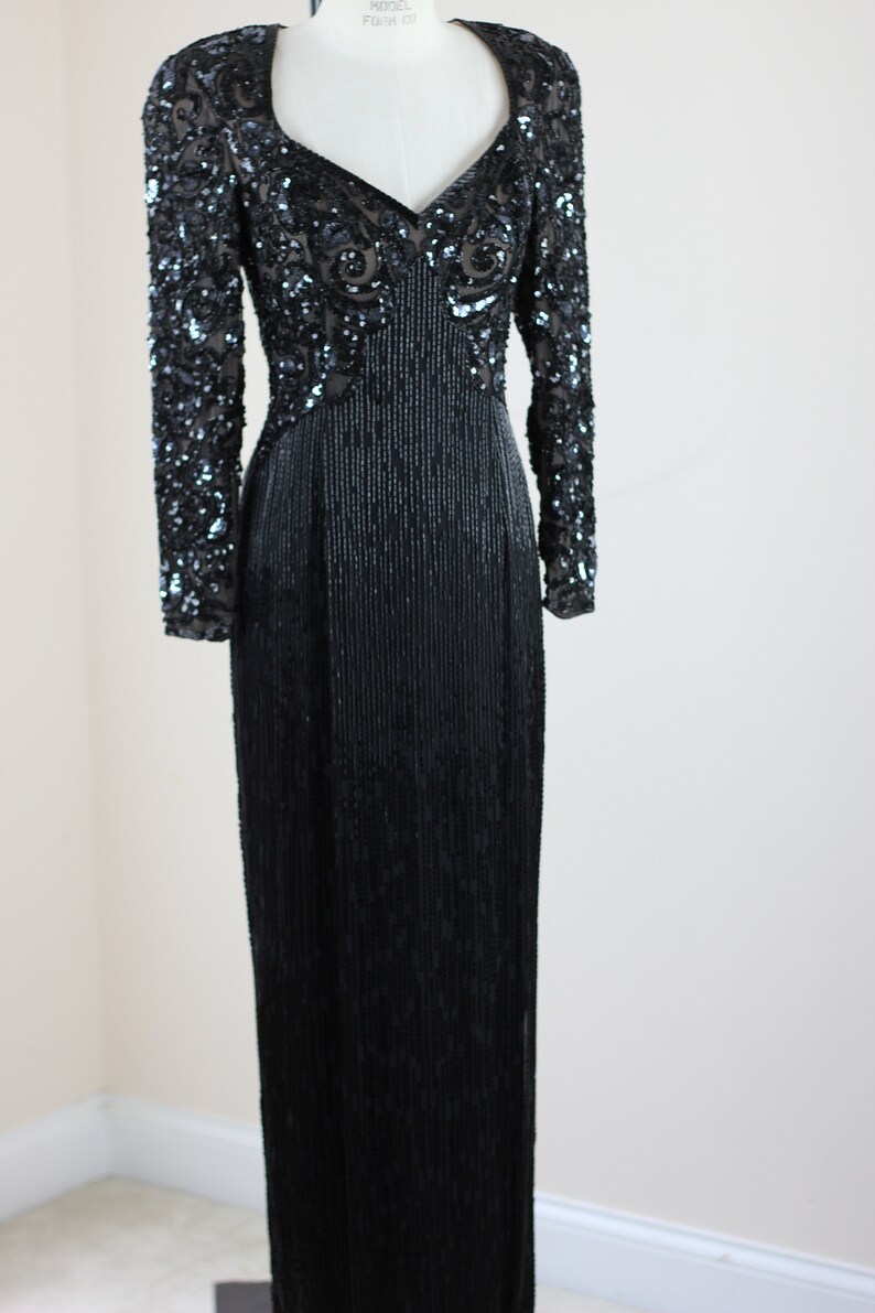 May include: A long-sleeved black sequined dress with a V-neckline and a fitted silhouette. The dress features intricate beading and sequins throughout, creating a glamorous and elegant look.