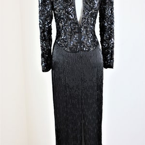 May include: A black sequined evening gown with long sleeves and a deep V-back. The gown features a beaded fringe skirt.