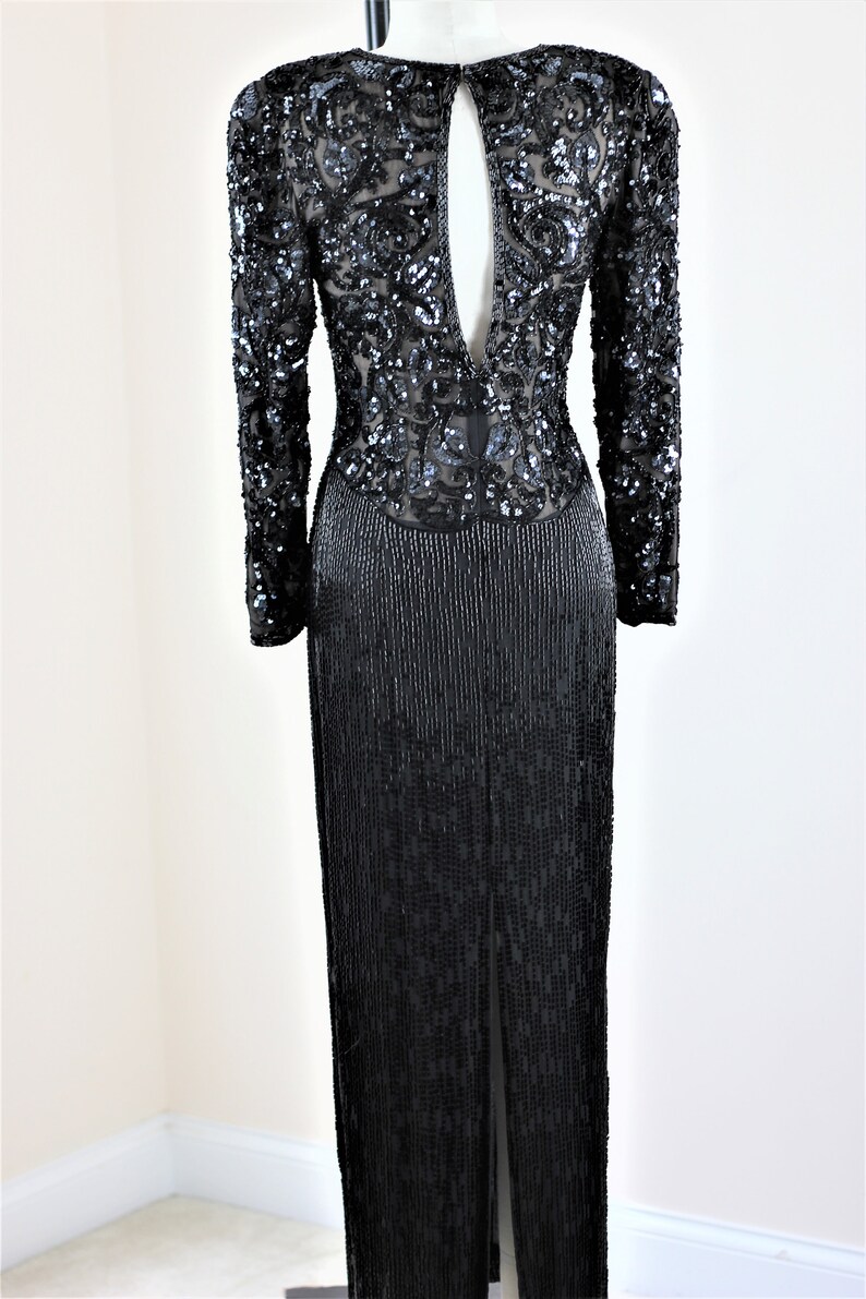May include: A black sequined evening gown with long sleeves and a deep V-back. The gown features a beaded fringe skirt.