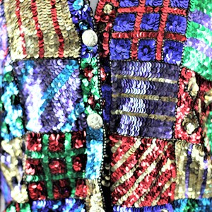 Puede incluir: Primer plano de un chaleco con lentejuelas con un dise&ntilde;o de patchwork. El chaleco presenta una variedad de colores que incluyen dorado, rojo, verde, azul y morado. El chaleco tiene cuello en V y se abrocha con tres botones plateados.