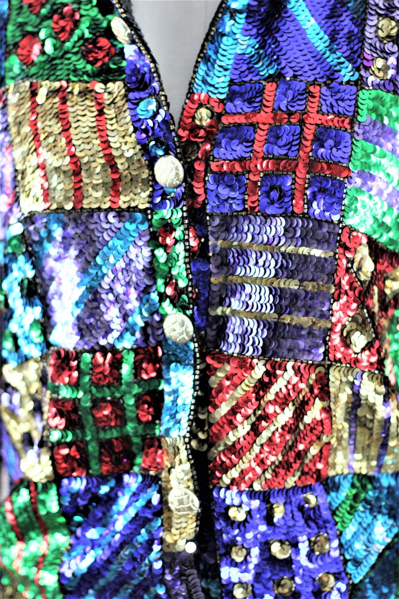 Puede incluir: Primer plano de un chaleco con lentejuelas con un dise&ntilde;o de patchwork. El chaleco presenta una variedad de colores que incluyen dorado, rojo, verde, azul y morado. El chaleco tiene cuello en V y se abrocha con tres botones plateados.