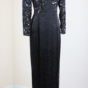 May include: A long black sequined evening gown with a V-neckline and long sleeves. The gown is fully sequined with a pattern of swirls and lines.